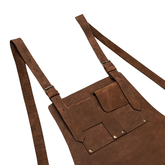 Premium cowhide leather grilling apron with dual towel rings and custom engraving options. Includes adjustable buckled straps, front storage pockets, and tool loops. Designed for hairstylists, chefs, handymen, and BBQ lovers. A thoughtful handmade leather gift for professionals or home cooks.